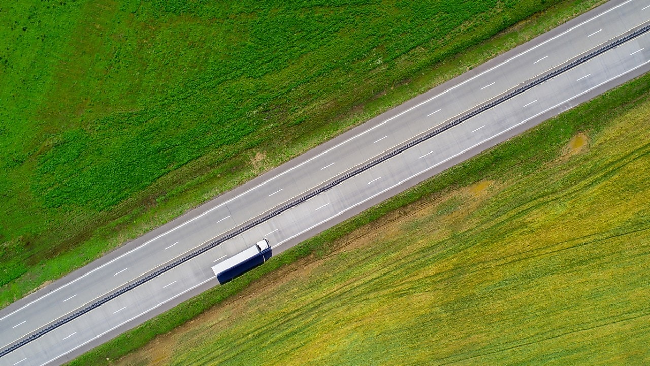 Een bovenaanzicht van een witte vrachtwagen op de snelweg in een groen landschap