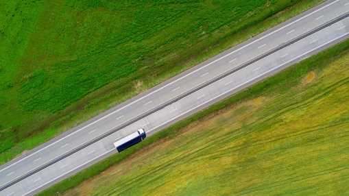 Een bovenaanzicht van een witte vrachtwagen op de snelweg in een groen landschap