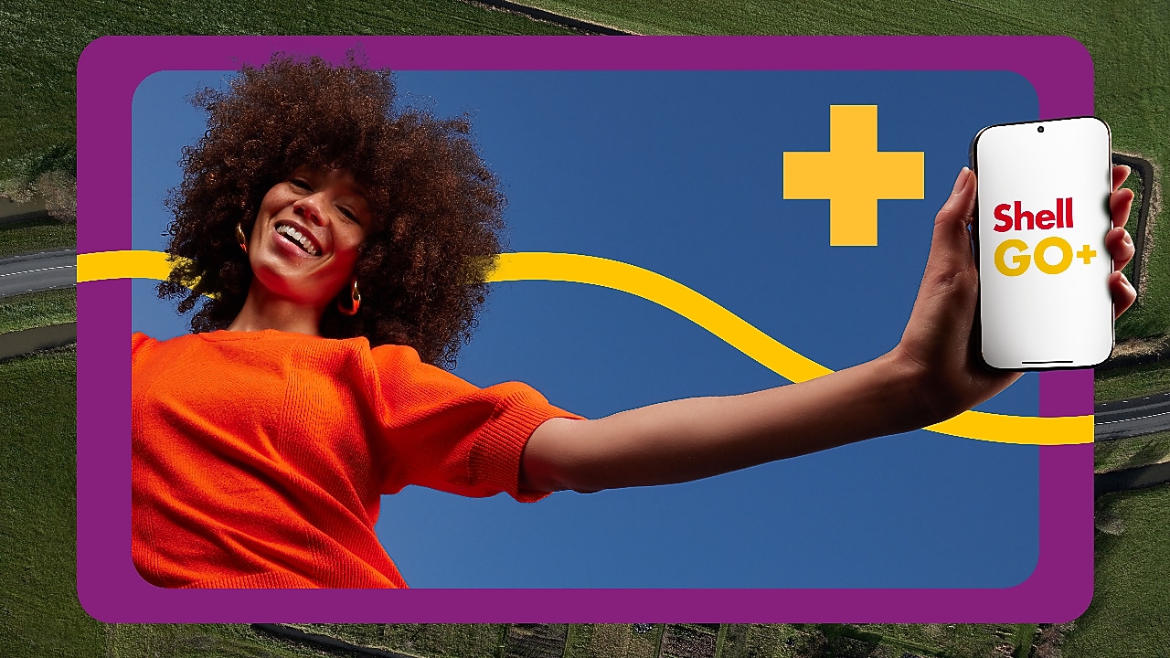 Een vrouw met oranje T-shirt houdt een mobiel vast met Shell GO+ erop