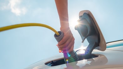 Een hand stopt een laadkabel in de elektrische auto.