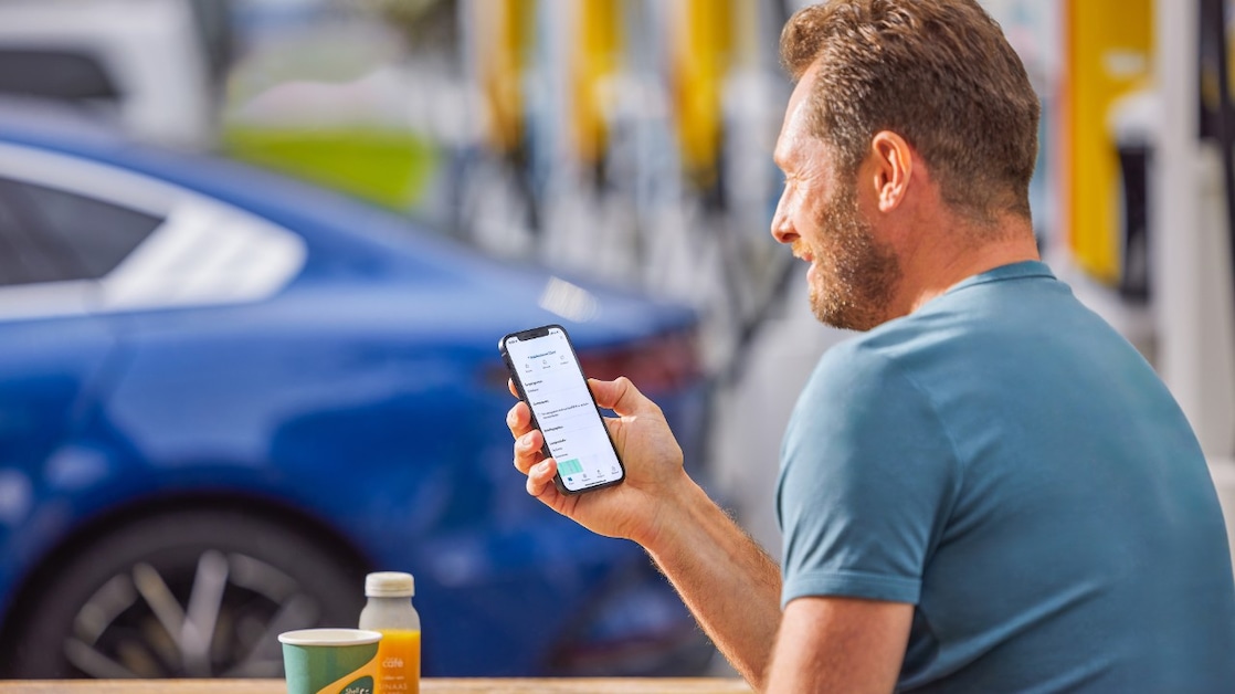 Een man kijkt op zijn mobiel terwijl zijn elektrische auto staat te laden.